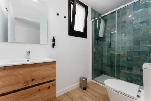 Baño moderno con tocador de madera, lavabo blanco, espejo con marco negro y ducha con azulejos verdes en Ab Be Apartments