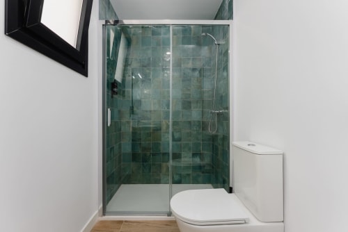 Baño moderno con ducha de azulejos verdes y inodoro blanco en los Apartamentos Ab Be, Málaga