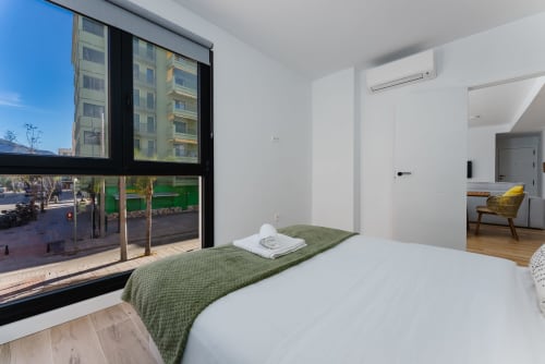 Habitación moderna en Ab Be Apartments en Málaga con gran ventana hacia la calle, colcha verde, sábanas blancas y