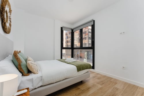 Dormitorio luminoso en Ab Be Apartments de Málaga con vistas al mar, cama con manta verde y ventana de marco negro con vistas a la ciudad