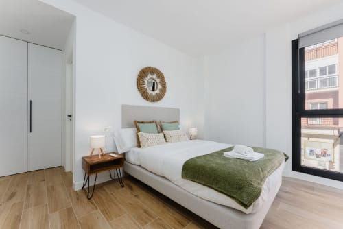 Habitación luminosa en Ab Be Apartments en Málaga con vistas al mar, cama blanca, manta verde, mesita de noche de madera y comodidades modernas