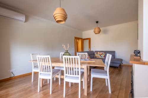 Sala de jantar moderna com cadeiras brancas e mesa de madeira no apartamento EcoHost, com vista para a sala de estar com sofá azul