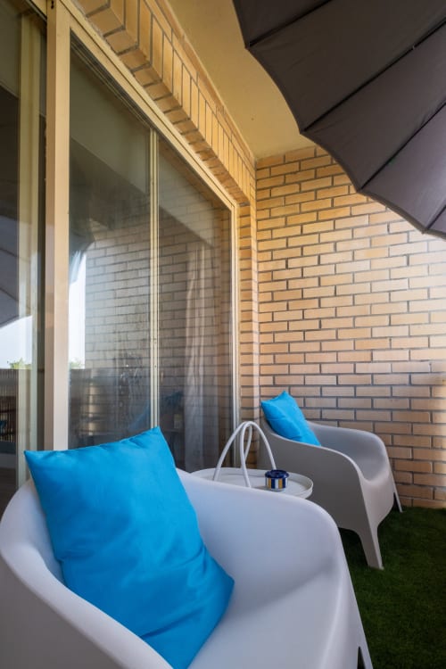 Varanda moderna no apartamento EcoHost Marina com cadeiras brancas, almofadas azuis, parede de tijolos e vista da cidade