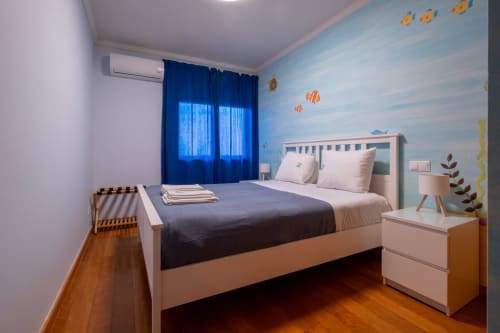 Quarto infantil moderno no apartamento EcoHost com painel de parede temático submarino, cama rosa, cortinas azuis e madeira