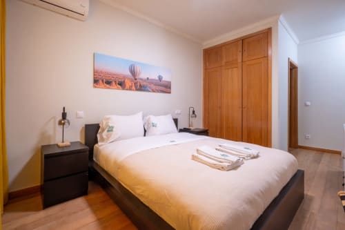 Quarto moderno no apartamento FamilyHub do EcoHost com cama de casal, criado-mudo preto, guarda-roupa de madeira e quadro com balão de ar quente