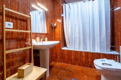 Banheiro moderno no EcoHost com azulejos cor de ferrugem, pia tipo coluna, vaso sanitário e banheira com cortina de chuveiro