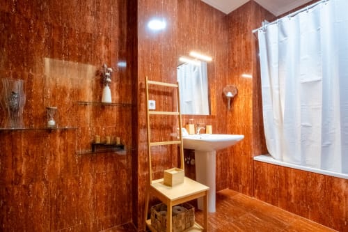 Banheiro moderno no apartamento EcoHost FamilyHub com paredes texturizadas tom ferrugem, pia de coluna, espelho e cortina de chuveiro branca