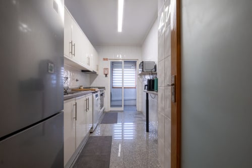 Cozinha compacta moderna no apartamento EcoHost FamilyHub com armários brancos, eletrodomésticos em aço inoxidável e iluminação LED