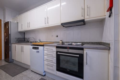 Cozinha moderna no apartamento EcoHost FamilyHub com armários brancos, bancada em granito, eletrodomésticos em aço inoxidável e vista da cidade