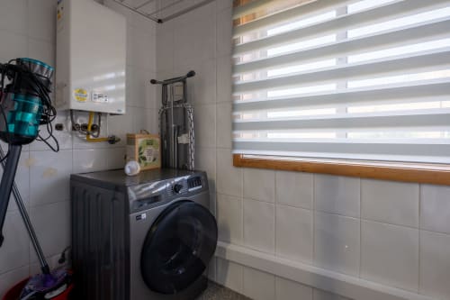 Lavandaria EcoHost com máquina de lavar preta, caldeira de parede, bicicleta e cortinas listradas coloridas