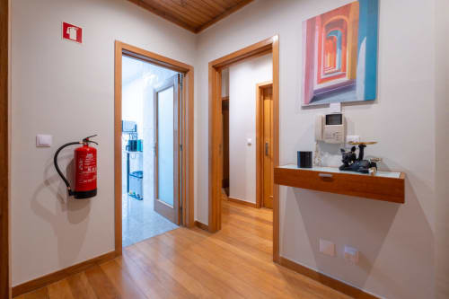 Corredor moderno do apartamento EcoHost FamilyHub em Portugal com portas em madeira, equipamentos de segurança e arte contemporânea