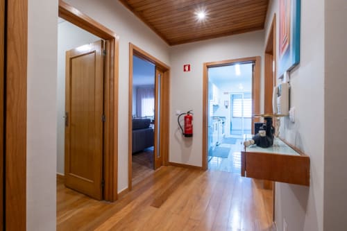 Corredor moderno do apartamento FamilyHub com portas, piso e teto em madeira; extintor de incêndio na parede; acesso à cozinha