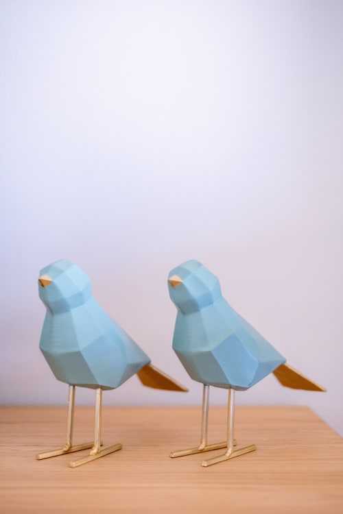 Duas decorações geométricas de pássaros azuis com bicos dourados e patas de latão em mesa de madeira em quarto moderno de hotel
