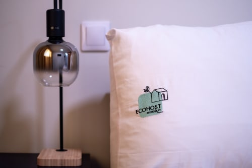 Quarto de apartamento EcoHost com luminária de design moderno e pacote de comodidades ecológicas em roupa de cama branca