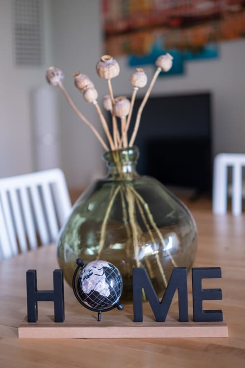 Placa HOME com globo decorativo ao lado de vaso de vidro com flores secas sobre mesa de madeira no apartamento EcoHost
