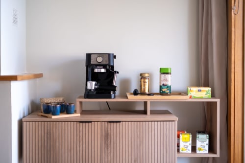 Cozinha do apartamento EcoHost com máquina de espresso, suprimentos de café, e prateleiras de madeira com utensílios e itens de despensa