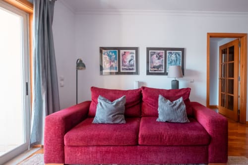 Sala luminosa com sofá vermelho vibrante, almofadas azuis listradas, cartazes de filmes vintage e porta de madeira no apartamento EcoHost