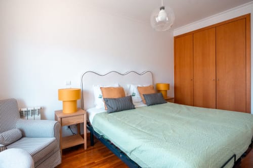 Quarto moderno no apartamento EcoHost OceanGreen com cama queen, guarda-roupa em madeira laranja, luminária amarela e vista para o jardim