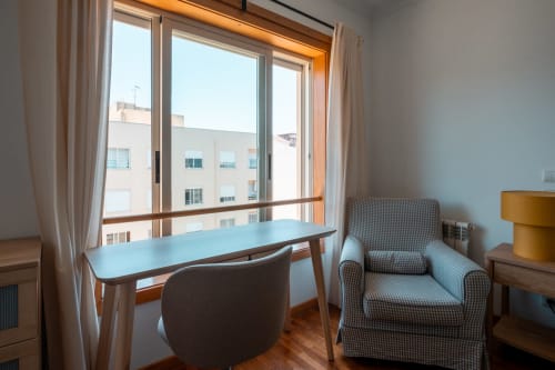 Área de estar moderna com espaço de trabalho, poltrona e janelas com vista para o jardim da EcoHost Portugal