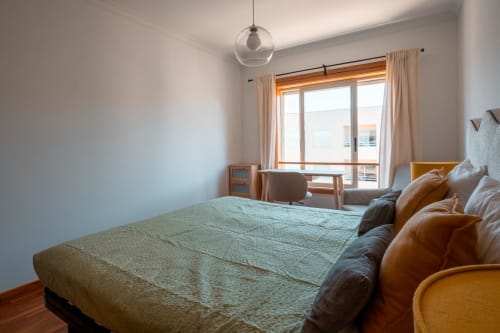 Quarto moderno e luminoso na EcoHost com cama verde, sofá de couro, luminária pendente e vista para o oceano