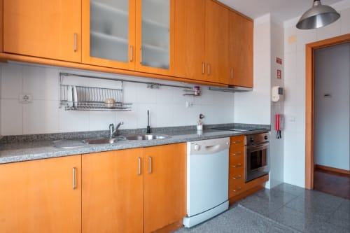 Cozinha moderna com armários laranja, bancadas cinzas, eletrodomésticos em aço inoxidável e azulejos brancos no apartamento EcoHost em