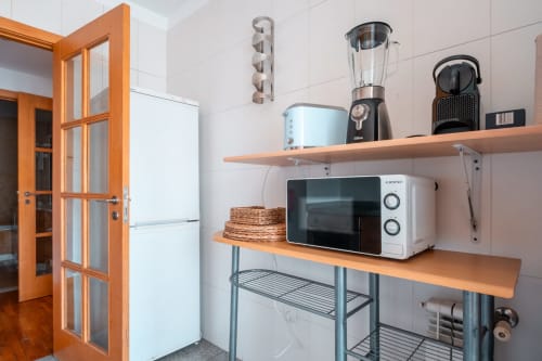 Cozinha moderna com prateleiras de madeira, micro-ondas, liquidificador e cafeteira no apartamento EcoHost