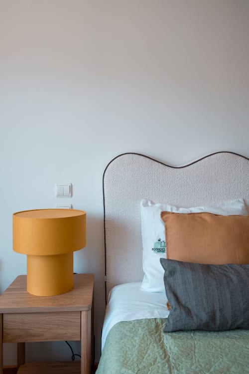 Quarto moderno no EcoHost com cabeceira estofada cinza, luminária amarelo mostarda e almofadas em tons neutros