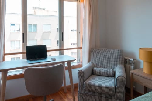Espaço de trabalho moderno em apartamento com laptop na mesa junto à janela com vista para o jardim, poltrona listrada e móveis de madeira na EcoHost