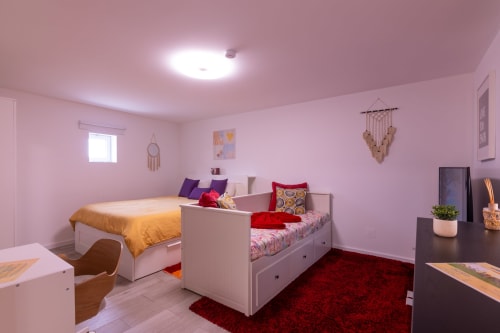 Quarto compartilhado rosa vibrante com duas camas brancas, almofadas coloridas, tapete vermelho e luz natural na Perafita Yellow House