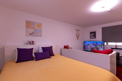 Quarto rosa vibrante com cama amarela, almofadas roxas, TV e vista para o jardim no eco apartamento Perafita Yellow House em Portugal