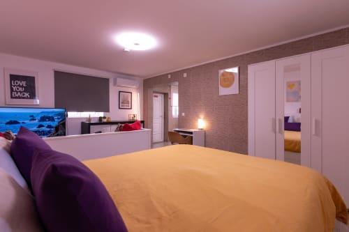 Quarto moderno com roupa de cama amarela e almofadas roxas na EcoHost Perafita Yellow House, paredes rosa e parede de tijolos