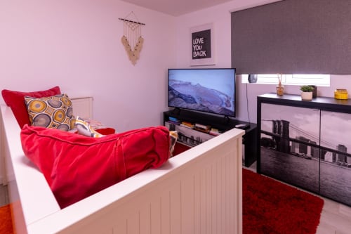 Quarto moderno com paredes rosa, roupa de cama vermelha, TV, móveis pretos e almofadas coloridas no apartamento EcoHost em Portugal