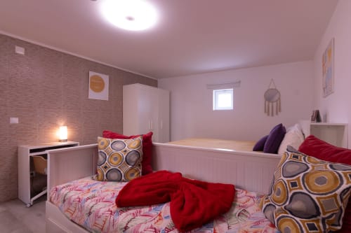 Quarto rosa vibrante com camas de solteiro, almofadas vermelhas, guarda-roupa branco e parede de tijolos na EcoHost Perafita