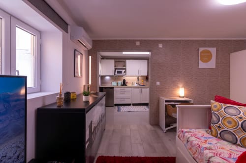 Estúdio moderno na Perafita Yellow House com paredes rosa, cozinha equipada, cama com roupa de cama estampada, TV e tijolos à vista