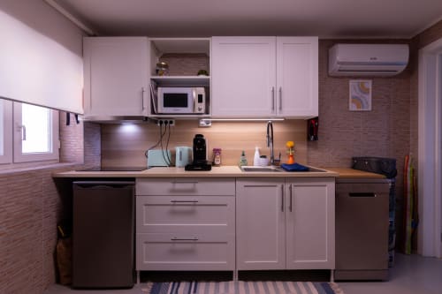 Cozinha moderna rosa com eletrodomésticos em aço inoxidável, paredes de tijolos e ar condicionado no apartamento EcoHost Perafita.