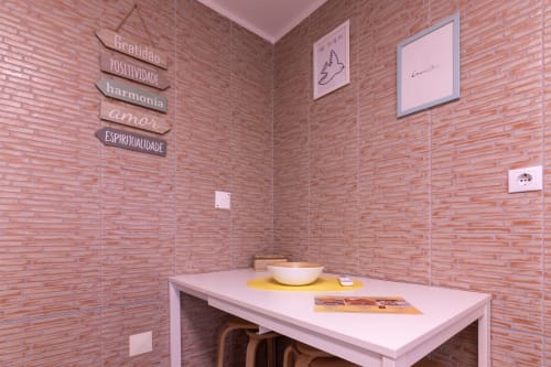 Quarto de tijolos rosa no EcoHost com placas motivacionais em português na parede, mesa branca com tigela e quadros decorativos