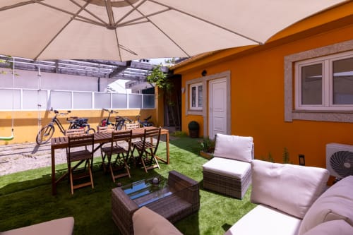 Terraço de jardim amarelo vibrante com área de estar, mesa de jantar, guarda-sol, bicicletas e gramado verde na EcoHost Portugal