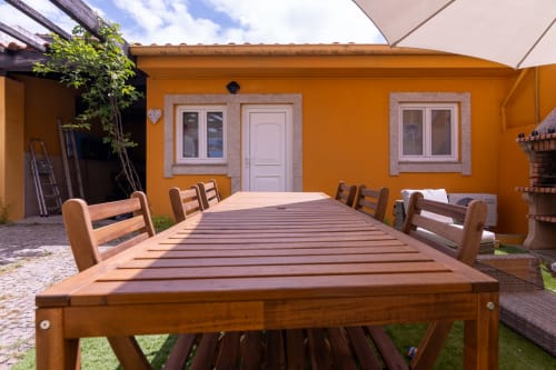 Mesa de jantar em madeira na varanda ensolarada da Casa Amarela de Perafita com fachada laranja e cadeiras