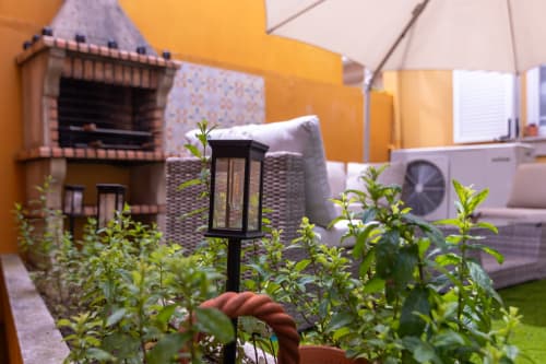 Pátio ensolarado com espreguiçadeira, plantas, luminária solar e sombrinha na EcoHost Perafita Yellow House