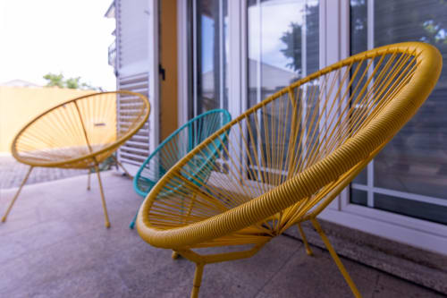 Espreguiçadeiras amarelas de fibra trançada no terraço da EcoHost Perafita Yellow House, com portas de vidro e vistas para as montanhas ao fundo