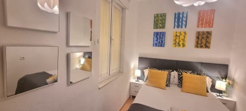 Moderno dormitorio en Casa Román Sport de León con almohadas amarillas, cabecero oscuro, espejo y obra de arte colorida en las paredes