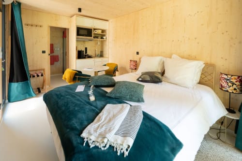 Modern wooden lodge bedroom at Le chant des pins with bed, kitchenette, and teal accents in Saint-Marc-Jaumegarde
