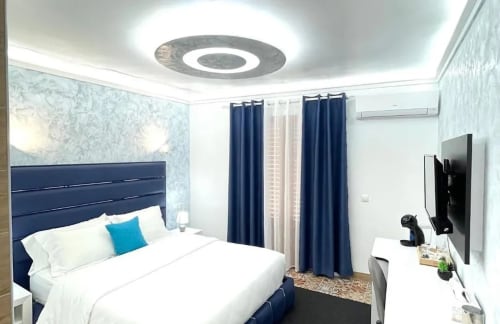 Moderno dormitorio doble en Hotel Boutique Galeon de Calpe con cabecero azul marino, ropa blanca, cortinas azules y TV de pantalla plana
