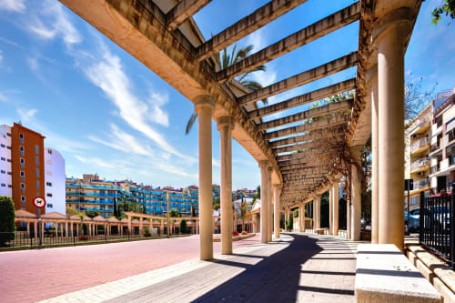 Galería porticada del Hotel Boutique Galeón en Calpe con plaza rosada, edificios azules y arquitectura mediterránea