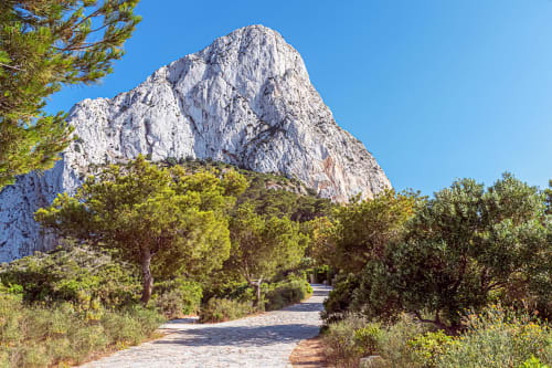 Camino de piedra con vista a acantilados de piedra caliza blanca en Calpe, vegetación mediterránea y cielo azul despejado