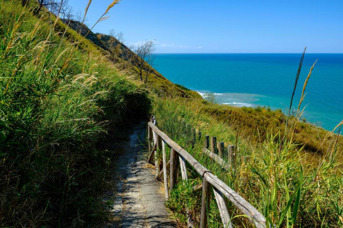 Sentiero con ringhiere in legno lungo la scogliera costiera con vista sul mare turchese vicino agli Appartamenti Riviera, Italia