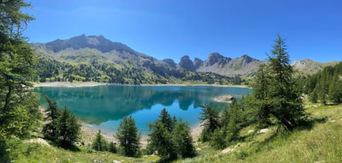 Turquoise alpine lake surrounded by forested mountains and green meadows near Hôtel la Source, La Foux