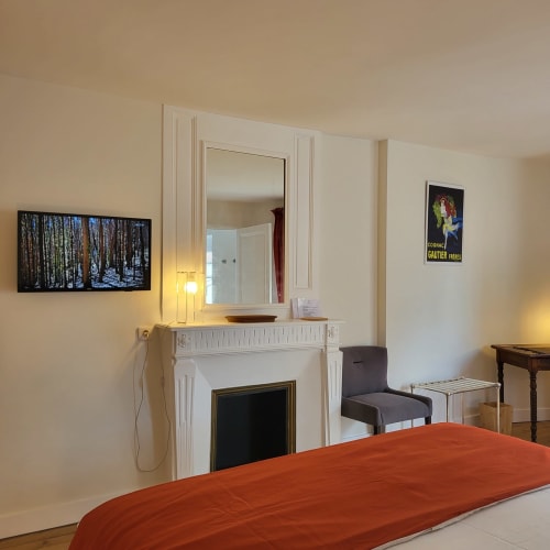 Élégante chambre Salignac aux Logis des Tourelles à Cognac, avec cheminée, miroir, literie rouge et vue sur la ville