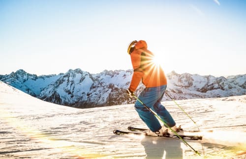 Skier in orange jacket on snowy slopes with snow-capped mountains at Hôtel la Source, La Foux