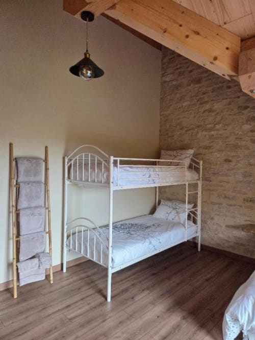 Chambre cosy avec lits superposés en métal blanc, poutres en bois et murs en pierre à La R'Mise de Surcey
